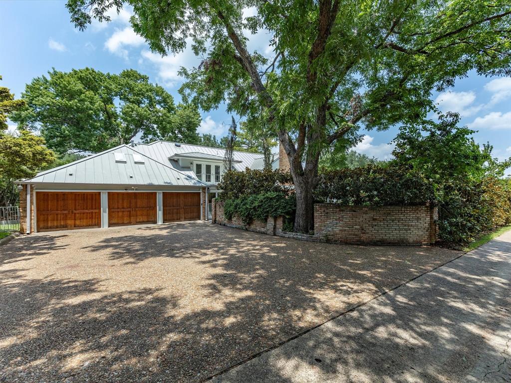 6160 Spring Valley Road Dallas, TX 75240 - Photo 39 of 40 Three-car garage with wood-paneled doors, a metal roof, and skylights