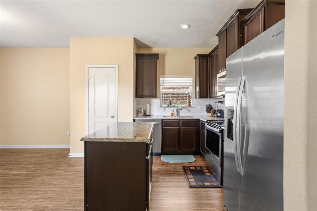 3005 Parker Road Anna, TX 75409 - Photo 9 of 33 Kitchen featuring stainless steel appliances, dark wood finish cabinetry, a center island, light stone counters, and dark wood-type flooring
