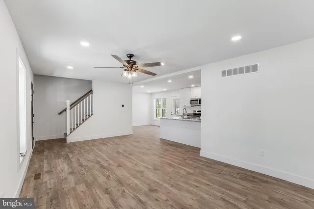 a view of an empty room with wooden floor and a ceiling fan