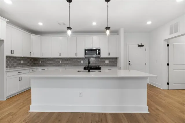 a view of kitchen with stainless steel appliances granite countertop sink stove and white cabinets with wooden floor