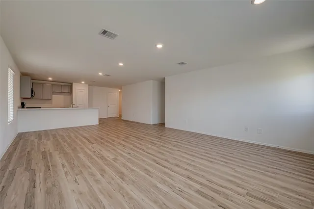 a view of an empty room with wooden floor and a kitchen
