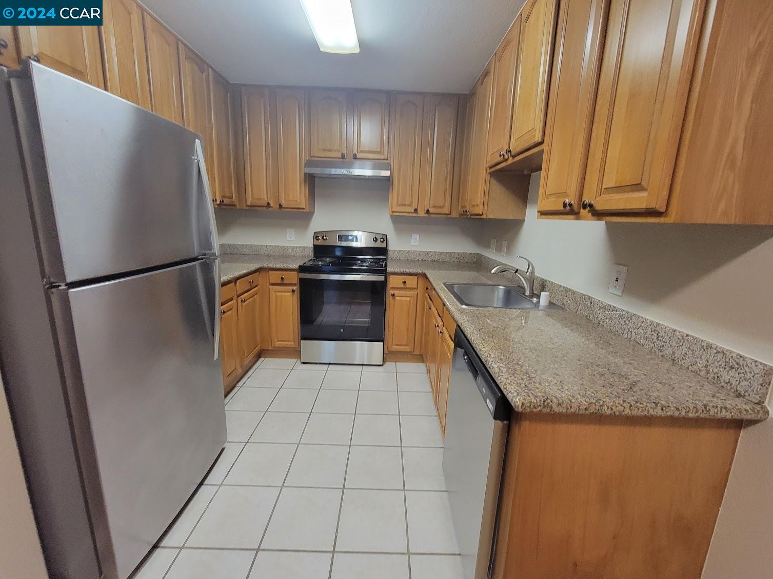 a kitchen with granite countertop stainless steel appliances a refrigerator a sink a stove top oven and cabinets
