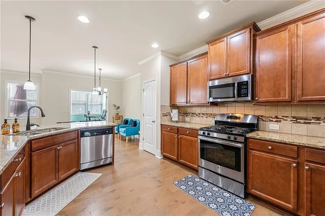 a large kitchen with stainless steel appliances granite countertop a stove top oven a sink dishwasher a dining table and chairs with wooden floor