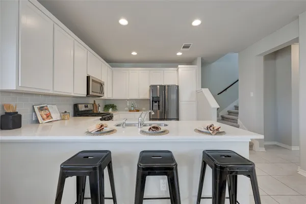 a kitchen with stainless steel appliances a sink a stove a refrigerator white cabinets and chairs
