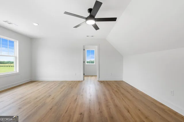 an empty room with wooden floor ceiling fan and windows