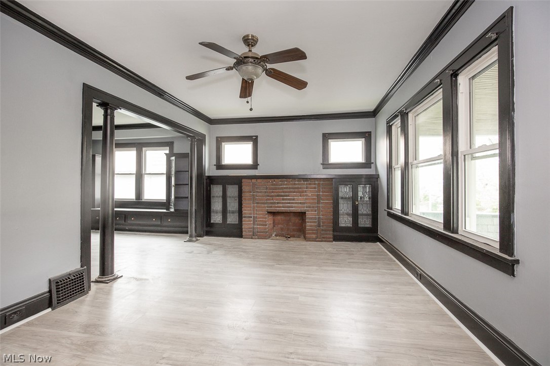 1868-1870 Lampson Road Cleveland, OH 44112 - Photo 4 of 36 Living area featuring light wood-finish flooring, a brick fireplace with built-in cabinetry, multiple windows with dark trim, dark crown molding, and a ceiling fan