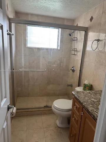 a bathroom with a granite countertop sink a toilet a window and shower