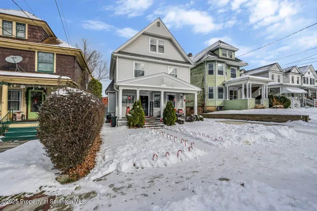 a view of a white house with large tree and wooden fence