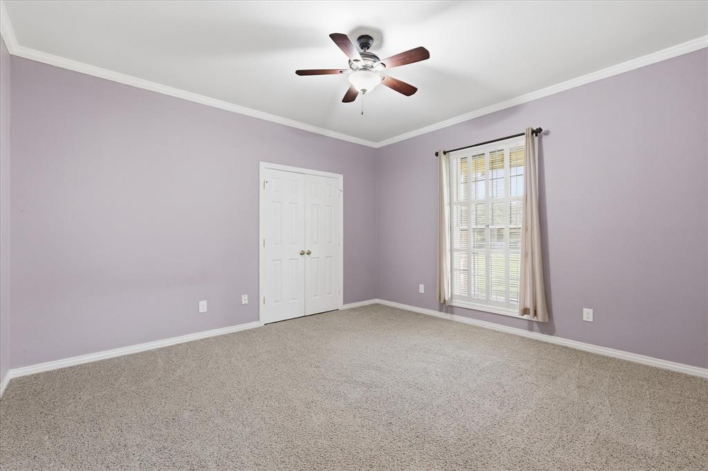 6955 Hawk Road Flower Mound, TX 75022 - Photo 29 of 40 Carpeted room with a ceiling fan, crown molding, double bi-fold closet doors, and a window with blinds and drapes