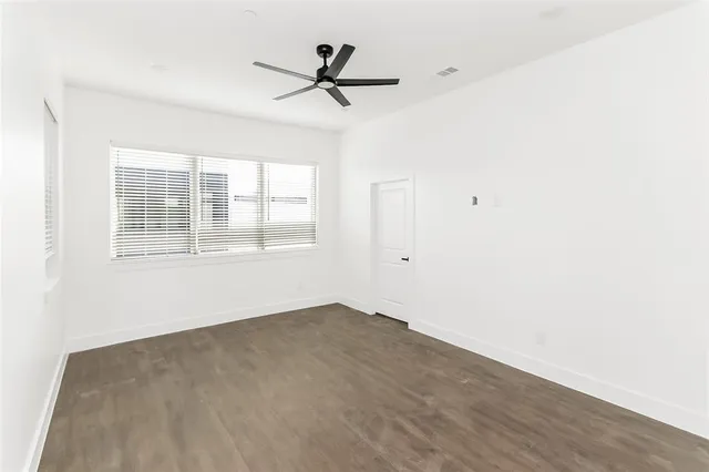 an empty room with wooden floor fan and windows