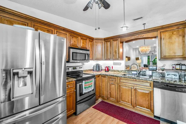 a kitchen with stainless steel appliances granite countertop a refrigerator a sink a stove and white cabinets with wooden floor