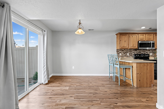 652 West 800 North, Unit 45 Clinton, UT 84015 - Photo 8 of 17 Open-concept living space featuring wood-finish flooring, a sliding glass door with exterior access, and a kitchen island with seating