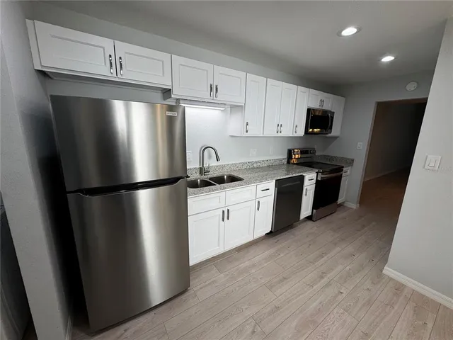 a kitchen with stainless steel appliances a refrigerator a sink a stove top oven and wooden floors