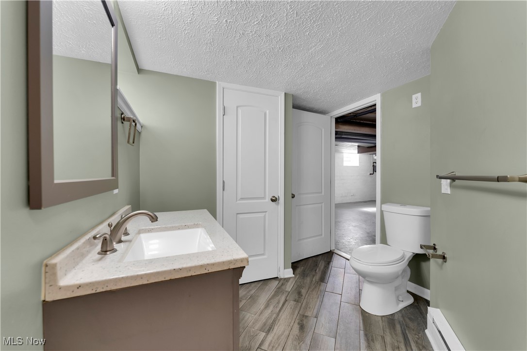 3739 Warren Road Cleveland, OH 44111 - Photo 9 of 40 Half bathroom featuring vanity, wood tiled floors, a baseboard radiator, and a textured ceiling