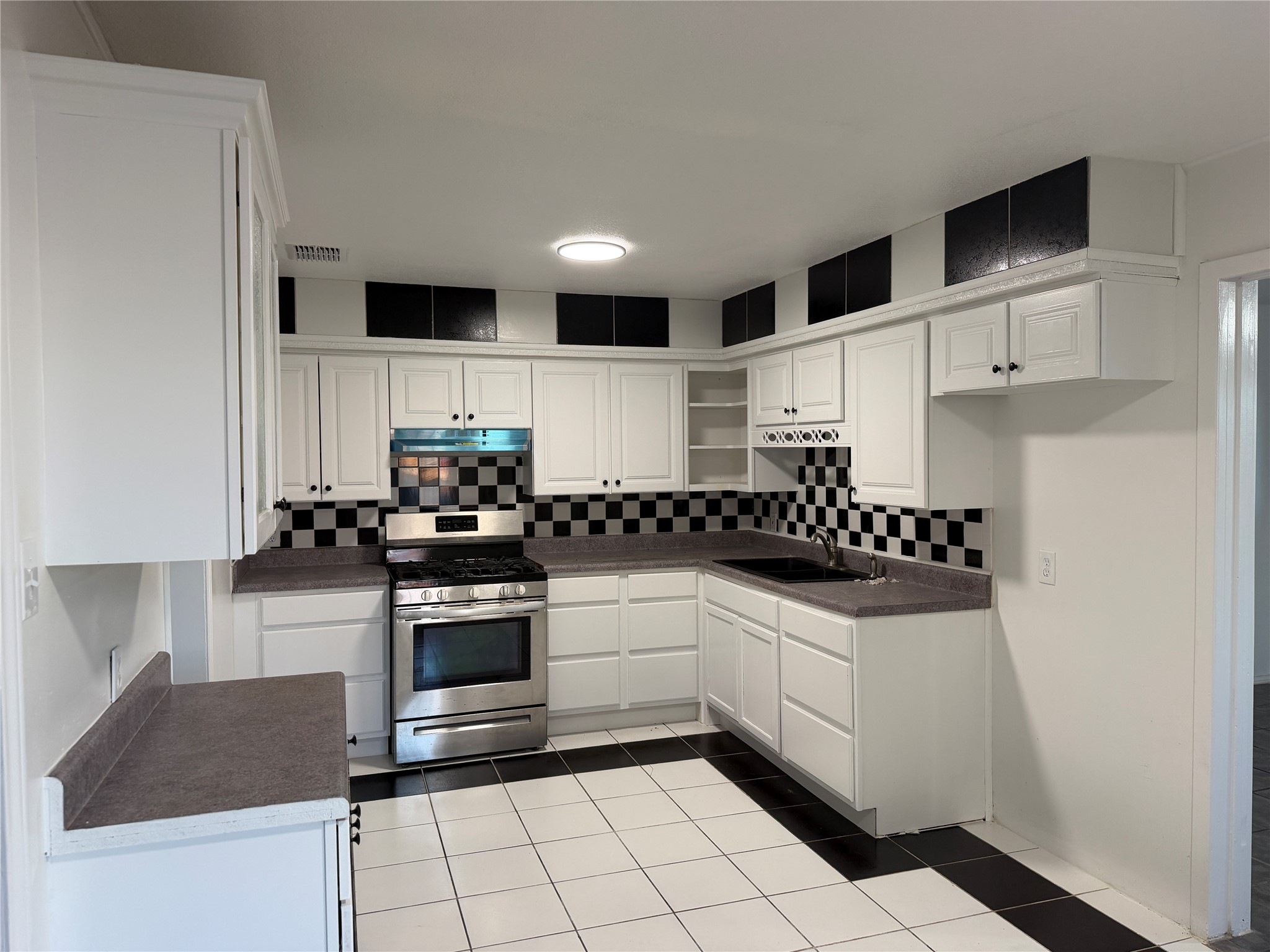1060 Gardner Road Austin, TX 78721 - Photo 12 of 19 White cabinetry, stainless steel appliances, and checkerboard details define this kitchen space.