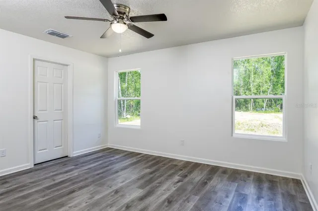 an empty room with wooden floor ceiling fan and windows