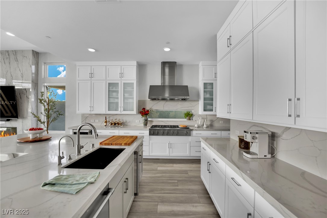 397 Highview Rdg Avenue Las Vegas, NV 89138 - Photo 40 of 97 Kitchen featuring white cabinets, light stone countertops, glass insert cabinets, decorative backsplash, and wall chimney range hood