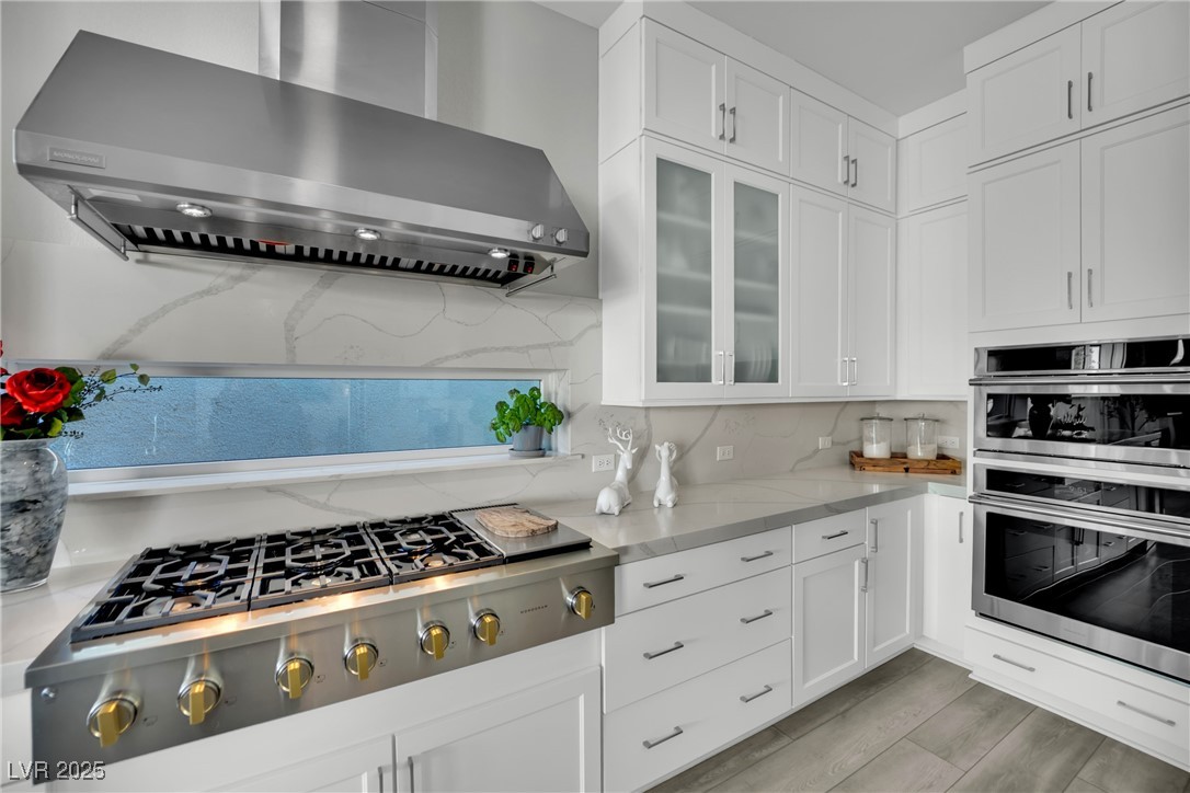 397 Highview Rdg Avenue Las Vegas, NV 89138 - Photo 43 of 97 Kitchen with wall chimney range hood, appliances with stainless steel finishes, white cabinetry, tasteful backsplash, and light stone countertops