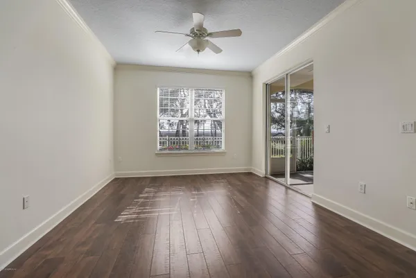 an empty room with wooden floor chandelier fan and windows