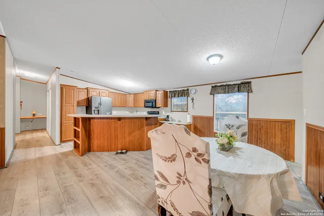 a living room with stainless steel appliances kitchen island granite countertop a refrigerator a sink a dining table and chairs with wooden floor