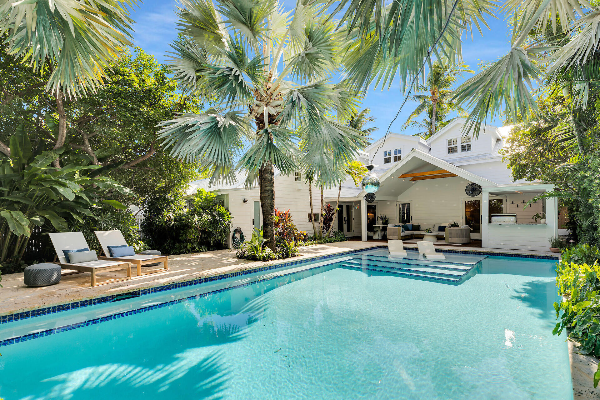 a view of a swimming pool with chairs and table and chairs under palm trees