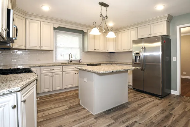 a kitchen with stainless steel appliances granite countertop a sink stove a refrigerator and white cabinets with wooden floor