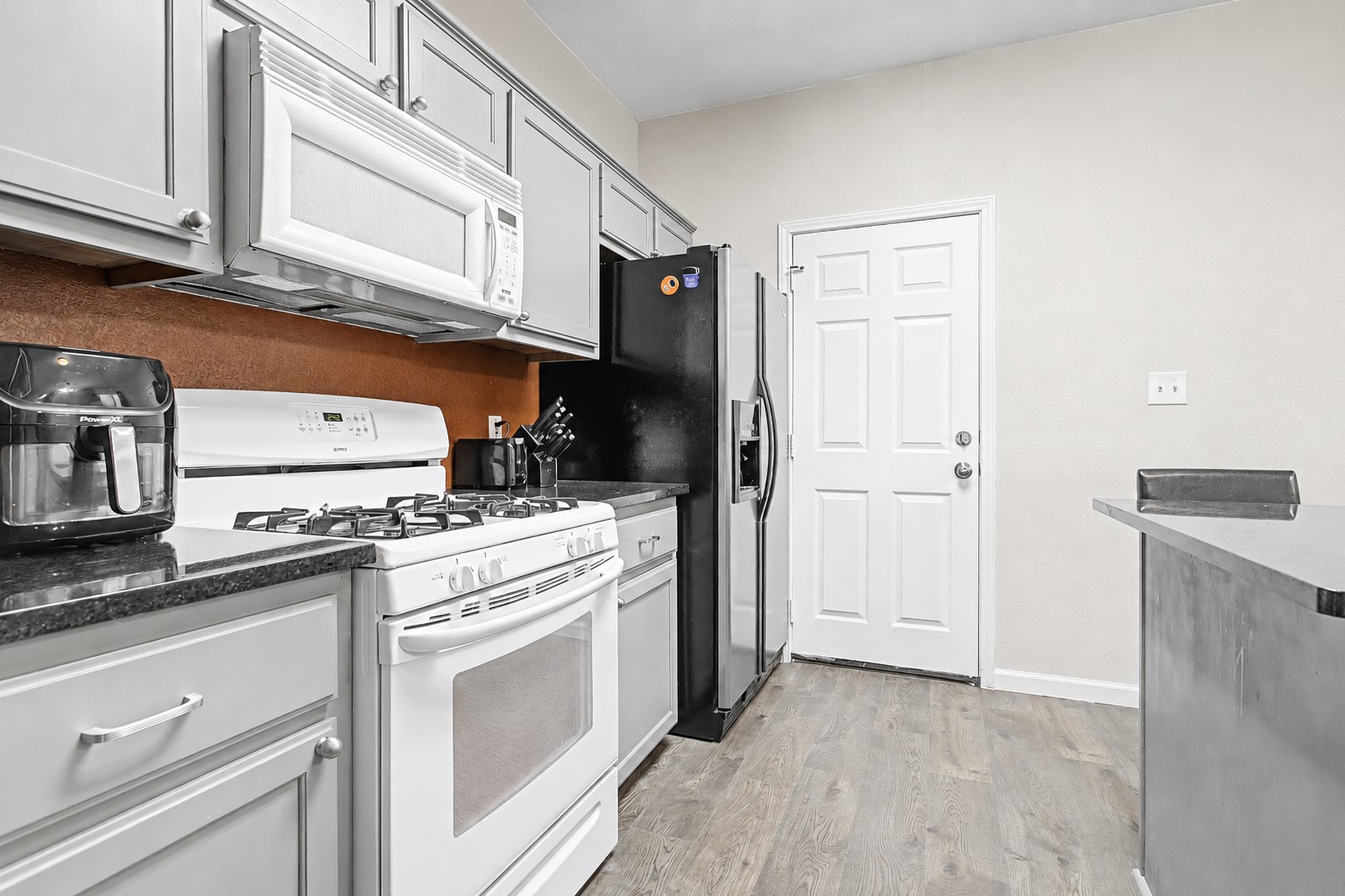 207 Kates Way Hutto, TX 78634 - Photo 4 of 24 Kitchen featuring light gray cabinetry, dark countertops, white appliance suite, and wood-finish flooring.
Photo digitally edited to remove personal items.