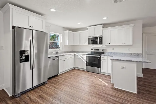 a kitchen with granite countertop a stove top oven a sink dishwasher and a refrigerator with wooden floor