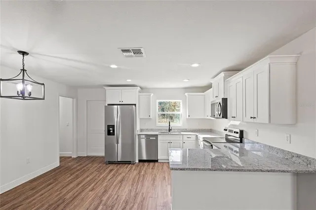 a kitchen with stainless steel appliances granite countertop a sink dishwasher a stove and a refrigerator with wooden floor