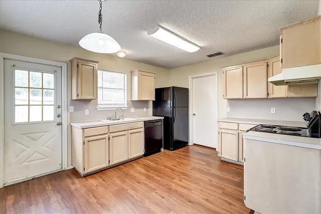 a kitchen with stainless steel appliances granite countertop a stove a sink dishwasher a refrigerator and white cabinets with wooden floor