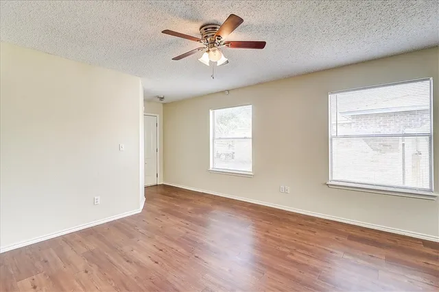 an empty room with wooden floor chandelier fan and windows