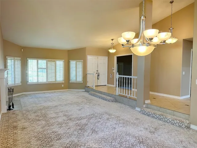 a view of an empty room with a chandelier fan and kitchen view
