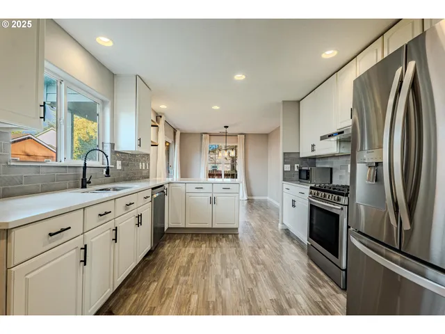 a kitchen with stainless steel appliances granite countertop a refrigerator a sink dishwasher a stove and white countertops with wooden floor