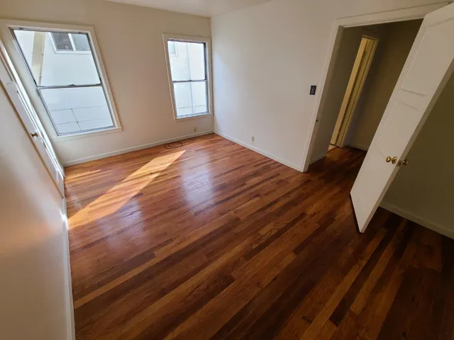 a view of empty room with wooden floor and fan