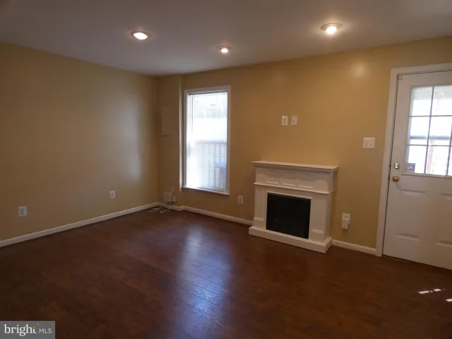 an empty room with wooden floor fireplace and windows