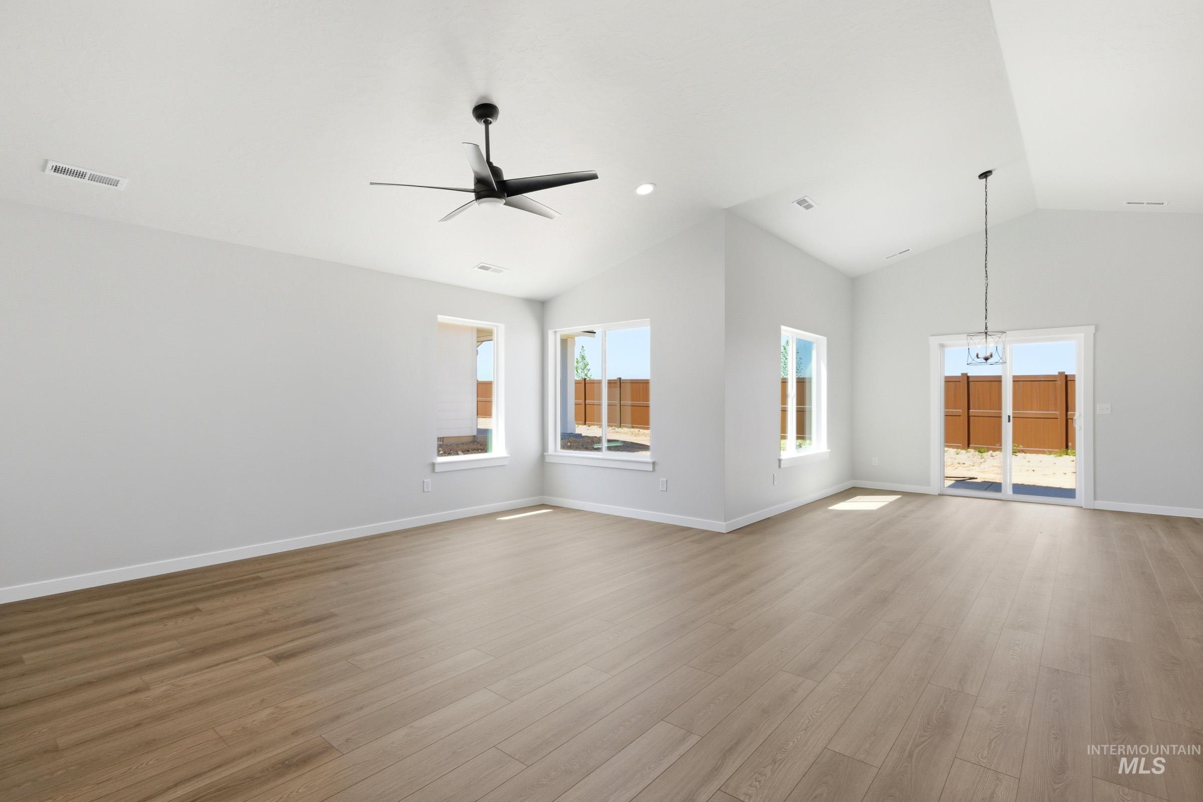 1184 West Jasper Street Meridian, ID 83642 - Photo 8 of 18 Spacious interior featuring vaulted ceilings, wood-finish flooring, multiple windows, a contemporary ceiling fan, and a glass sliding door leading to an outdoor space
