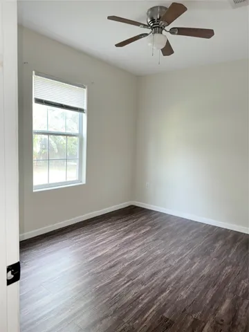 an empty room with wooden floor fan and windows
