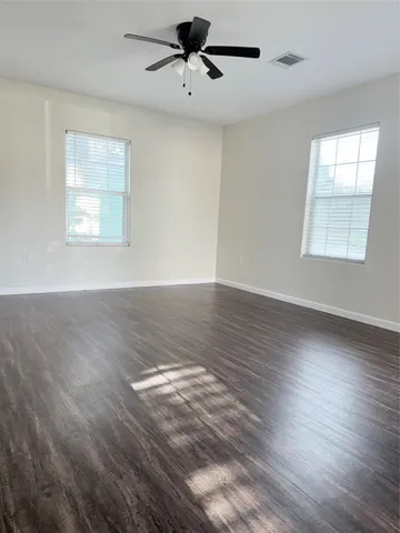 an empty room with wooden floor fan and windows