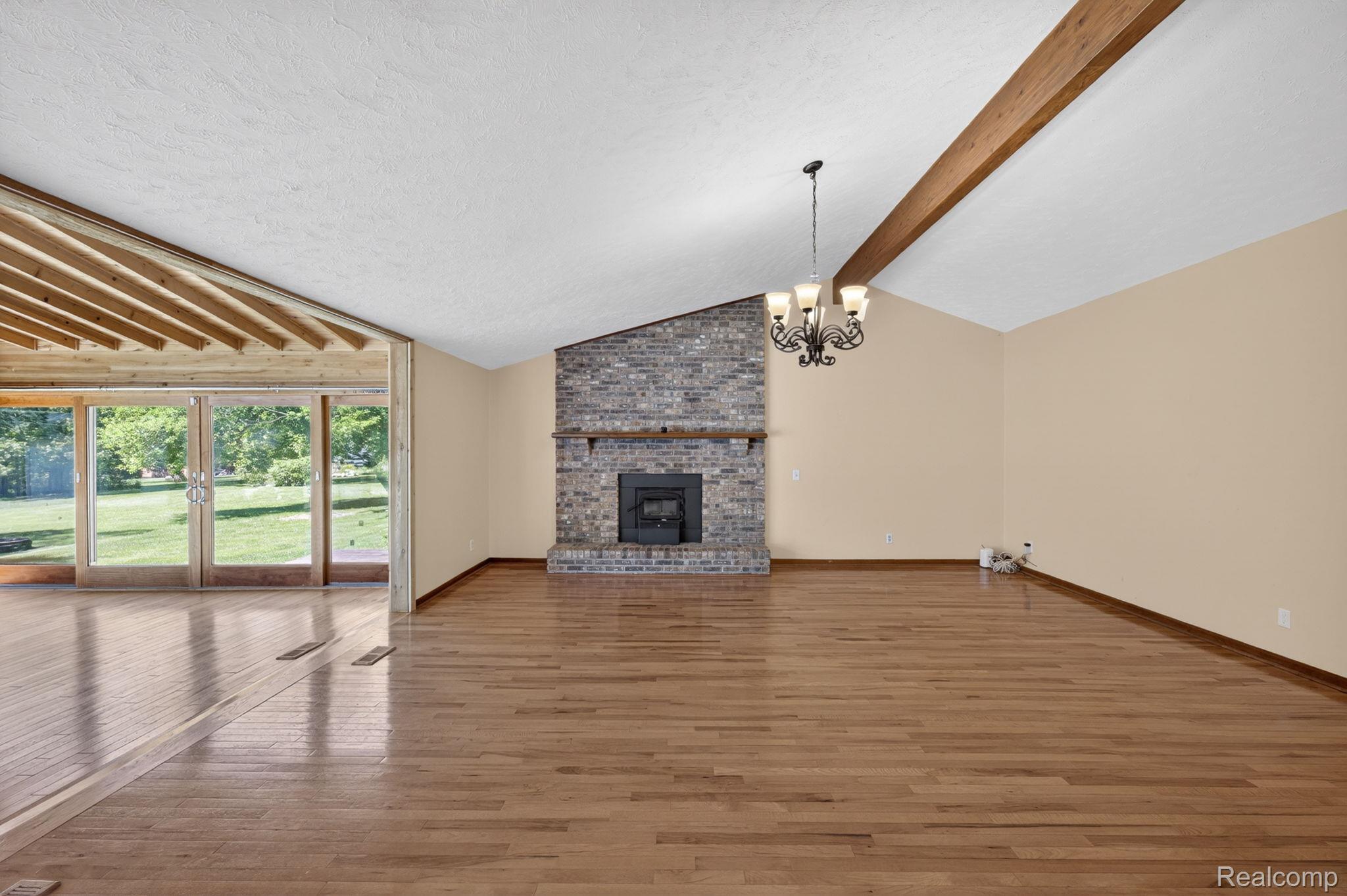 9353 Hill Road Swartz Creek, MI 48473 - Photo 27 of 98 Spacious room featuring vaulted ceilings with a visible wood beam, a stone fireplace with a wood mantel, and wood-finish flooring