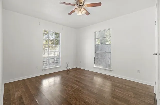an empty room with wooden floor chandelier fan and windows