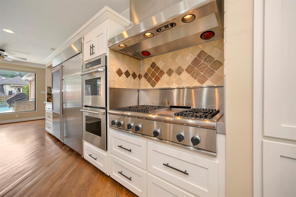 4008 Ramsgate Court Colleyville, TX 76034 - Photo 9 of 33 Gourmet kitchen featuring a professional-grade stainless steel range with griddle, ornate tile backsplash, integrated stainless steel appliances, white cabinetry with dark hardware, and wood-finish flooring
