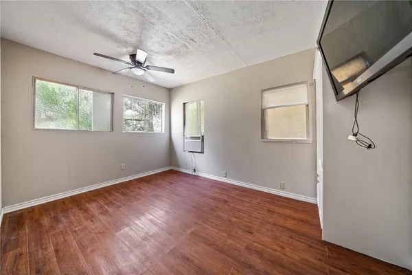 an empty room with wooden floor chandelier fan and windows