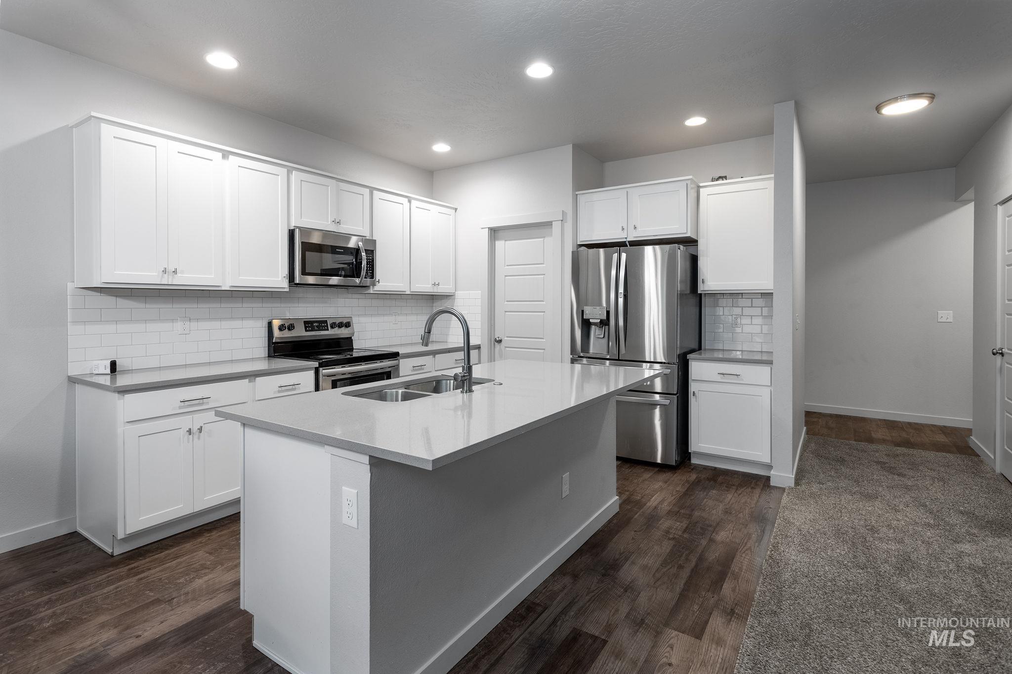 262 South Riggs Spg Avenue Meridian, ID 83642 - Photo 4 of 25 Kitchen featuring stainless steel appliances, white cabinetry, tasteful backsplash, a kitchen island with sink, and dark wood finished floors