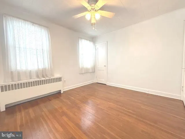 an empty room with wooden floor fan and windows