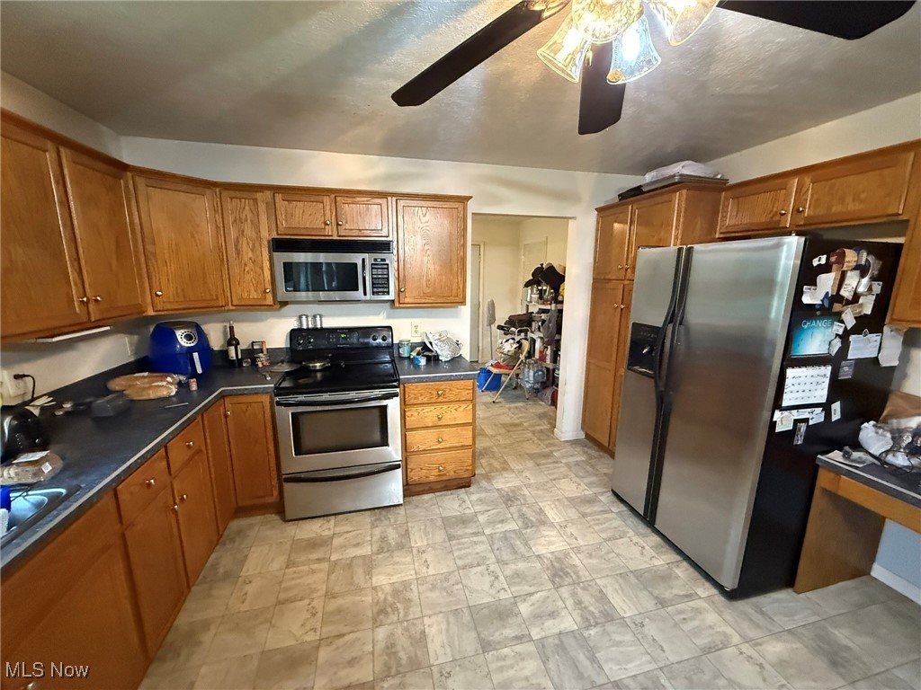 6920 Riverside Road Southeast Gnadenhutten, OH 44629 - Photo 9 of 41 Kitchen featuring stainless steel appliances, ceiling fan, dark countertops, and brown cabinets