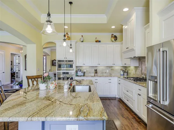a kitchen with kitchen island granite countertop a stove a sink a refrigerator and white cabinets with wooden floor