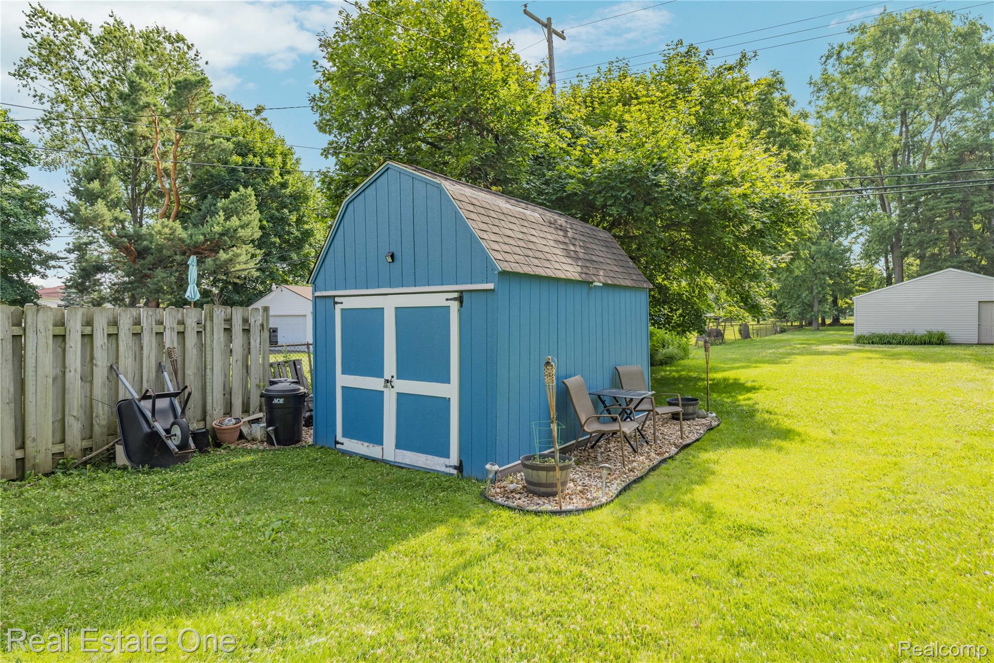 2810 Walbridge Drive Rochester, MI 48307 - Photo 44 of 58 Spacious backyard featuring a blue storage shed with white barn doors, a wooden privacy fence, a small rock-edged patio, and mature trees providing natural shade