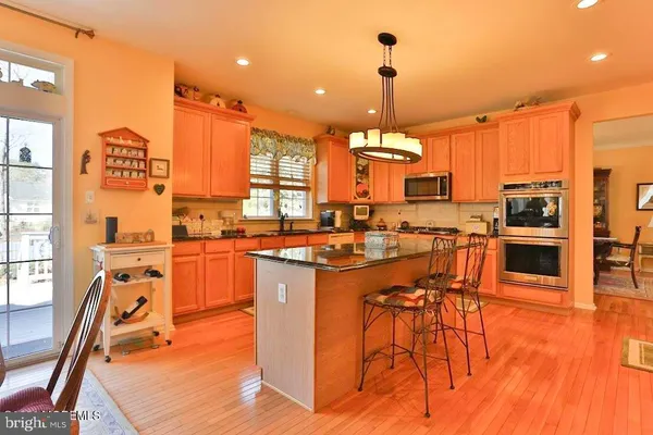 a kitchen with stainless steel appliances kitchen island granite countertop a stove top oven a sink a dining table and chairs with wooden floor