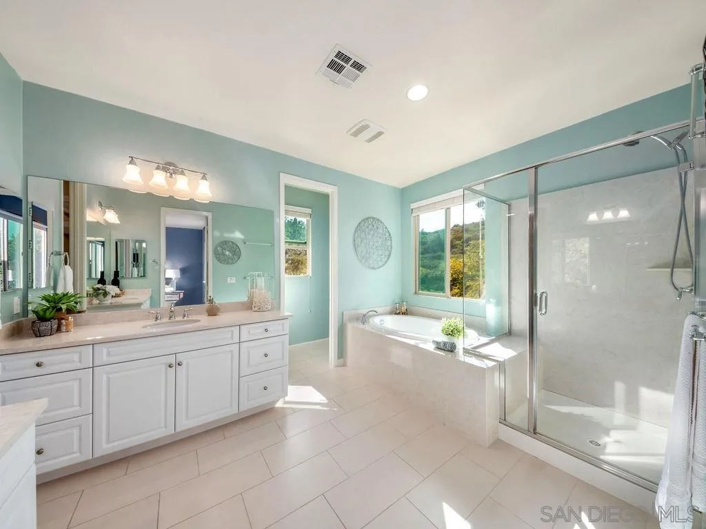 17568 Ralphs Ranch Road San Diego, CA 92127 - Photo 12 of 25 a spacious bathroom with a double vanity sink a large mirror a bathtub and next to a window