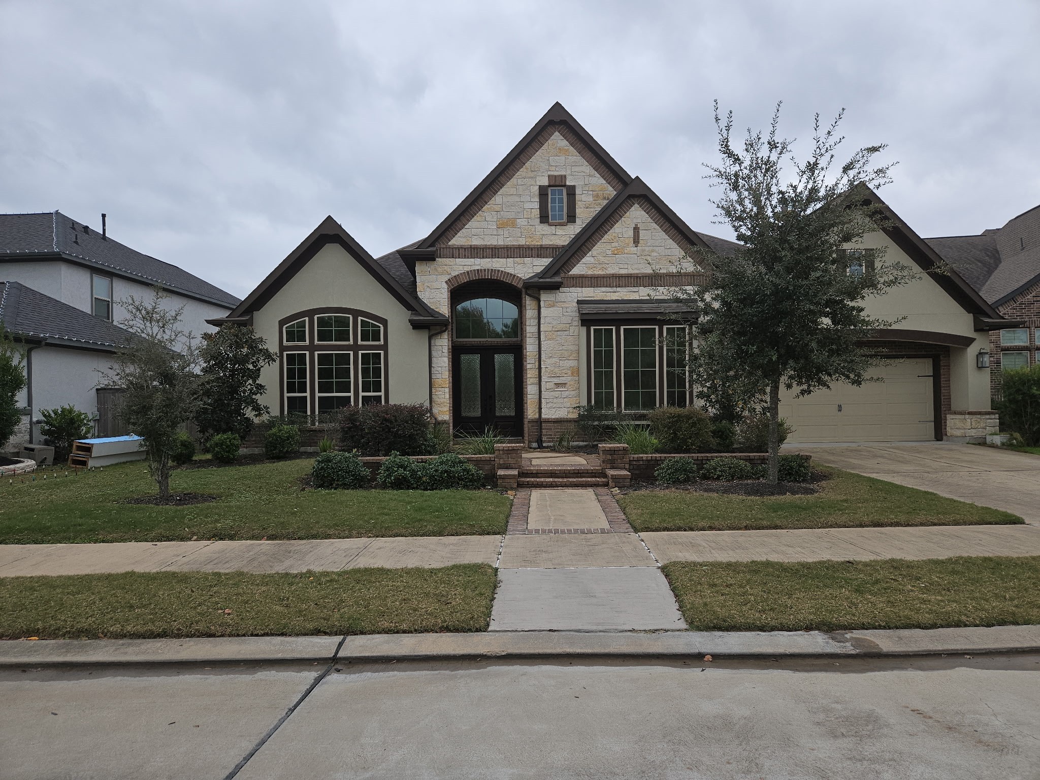 This is a charming, single-story home with a stone and brick exterior. It features a neatly landscaped front yard, large windows, and a welcoming front entrance. The attached garage complements its classic design.